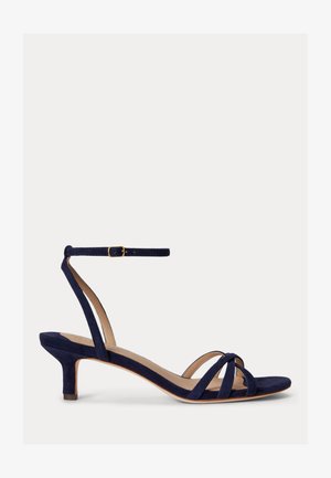 Σανδάλι από σουέντ σε ναυτικό μπλε με χαμηλό τακούνι τύπου kitten, λουράκι στον αστράγαλο με χρυσή αγκράφα και λεπτά λουριά που διασταυρώνονται πάνω από το δάχτυλο.