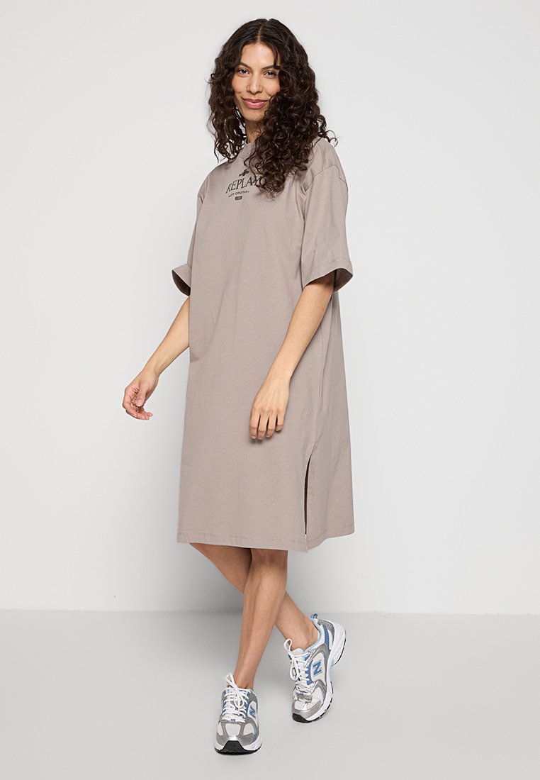 Oversized short-sleeve dress in beige cotton with a round neckline and side slit. Model paired it with gray and white sneakers.