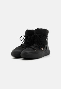 Zapatillas altas negras con parte superior de tela texturizada, puntera redonda y cierre de cordones. Presentan ojales en tono dorado y suela de goma.