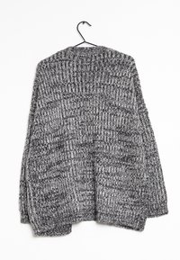 Stickad oversized cardigan i svart och grått. Har ett texturerat mönster, långa ärmar och en öppen design framtill. Hänger på en svart krok.