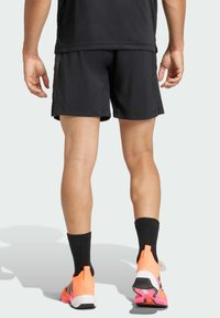 Pantalones cortos deportivos negros de corte holgado, combinados con zapatillas naranjas vibrantes y calcetines negros hasta la pantorrilla. Los pantalones cortos tienen una textura suave.