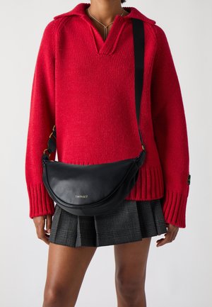 Punainen neulottu pusero kauluksella, musta nahkainen vyölaukku, jossa on kultainen logo, ja ruudullinen hame, jossa on laskokset. Yksinkertainen, toiminnallinen muotoilu.