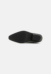 Suela de zapato negra con forma puntiaguda, goma texturizada para agarre y un diseño limpio y minimalista. Presenta un acabado suave y mate.
