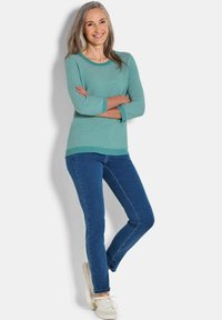 Türkise gestreifte Sweater mit Dreiviertelärmeln, kombiniert mit blauen Jeans und weißen Sneakern. Leichte Textur, lässige Passform, mit gerippten Akzenten.