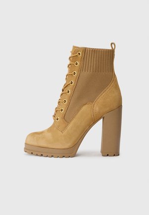 Tan lace-up ankle boots with gold eyelets, a textured knit upper, and a chunky heel. Features a solid toe and rugged sole.