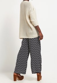 Světlý béžový pletený svetr s žebrovanými detaily, doplněný tmavě modrými širokými kalhotami s bílým květinovým vzorem a hnědými platformovými podpatky.