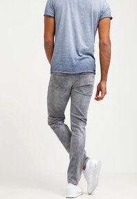 Vaqueros de mezclilla gris con un corte slim, que cuentan con bolsillos traseros y un sutil desgaste. Combinados con una camiseta azul claro y zapatillas blancas.