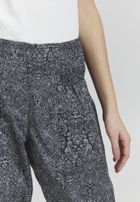 Marinblå byxor med vitt blommönster, med elastisk midja och en liten logodetalj. Lätt och luftig tygstruktur.