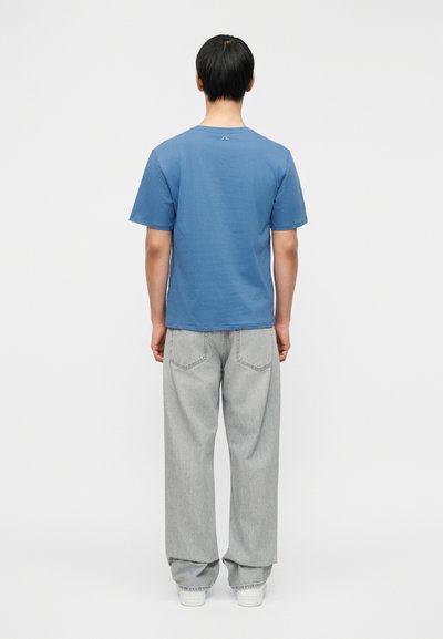 Μπλε βαμβακερό t-shirt με κοντά μανίκια και στρογγυλή λαιμόκοψη, συνδυασμένο με άνετο γκρι τζιν. Το σύνολο έχει μινιμαλιστικές σχεδιαστικές λεπτομέρειες.