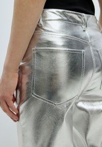 Metalen zilveren broek met een glad, reflecterend oppervlak, voorzien van twee achterzakken en gestikte details langs de naden.