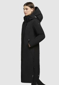 Sort lang parka med høj krave og aftagelig hætte, med sidelommer, glat stof og en figursyet silhuet.