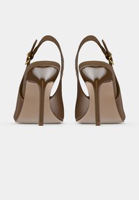 Καφέ ψηλοτάκουνα slingback παπούτσια με λεπτές στιλέτο γόβες, ορατές πόρπες και λείο φινίρισμα, εμφανιζόμενα από πίσω σε λευκό φόντο.