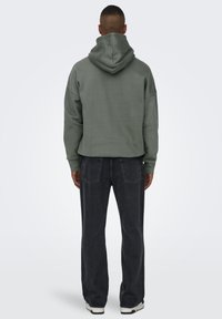 Cropped green hoodie with a drawstring hood, worn with dark denim jeans and white-soled sneakers. Simple design and relaxed fit.