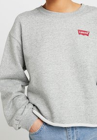 Grauer Pullover mit Rundhalsausschnitt und gerippten Bündchen, mit rotem Levi's-Logo-Tag auf der linken Brust. Baumwollmischgewebe, lockere Passform.