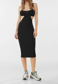 Svart midiklänning med utskärningar vid midjan. Tillverkad av mjukt material. Kombinerad med kraftiga sneakers.