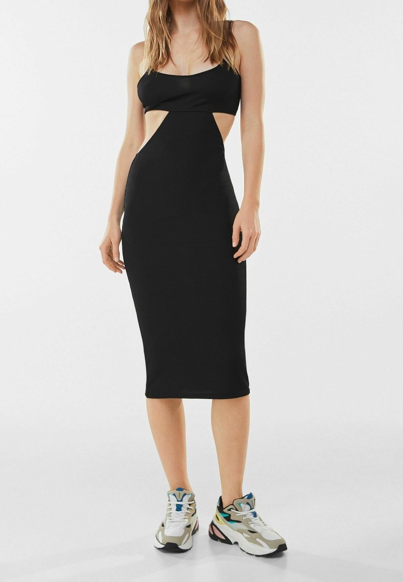 Svart midiklänning med utskärningar vid midjan. Tillverkad av mjukt material. Kombinerad med kraftiga sneakers.