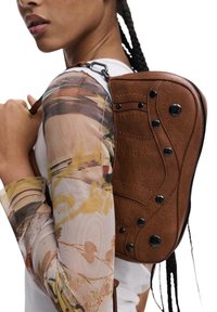 Zaino in pelle marrone con design testurizzato, cuciture decorative e accessori neri, indossato sulla schiena di un individuo. Motivo chiaro sulla manica.