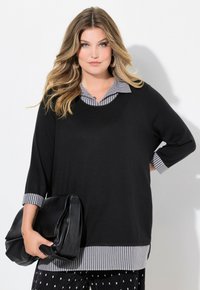 Maglione nero con maniche a tre quarti, dotato di collo e polsini a righe bianche e nere. Borsa in pelle nera tenuta davanti.