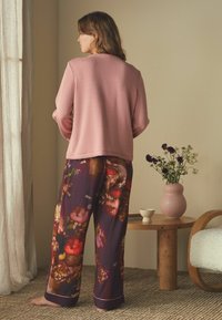 Lichtroze langemouwen top gecombineerd met donker gebloemde broeken in tinten paars, rood en roze. Gladde texturen en een relaxte pasvorm.