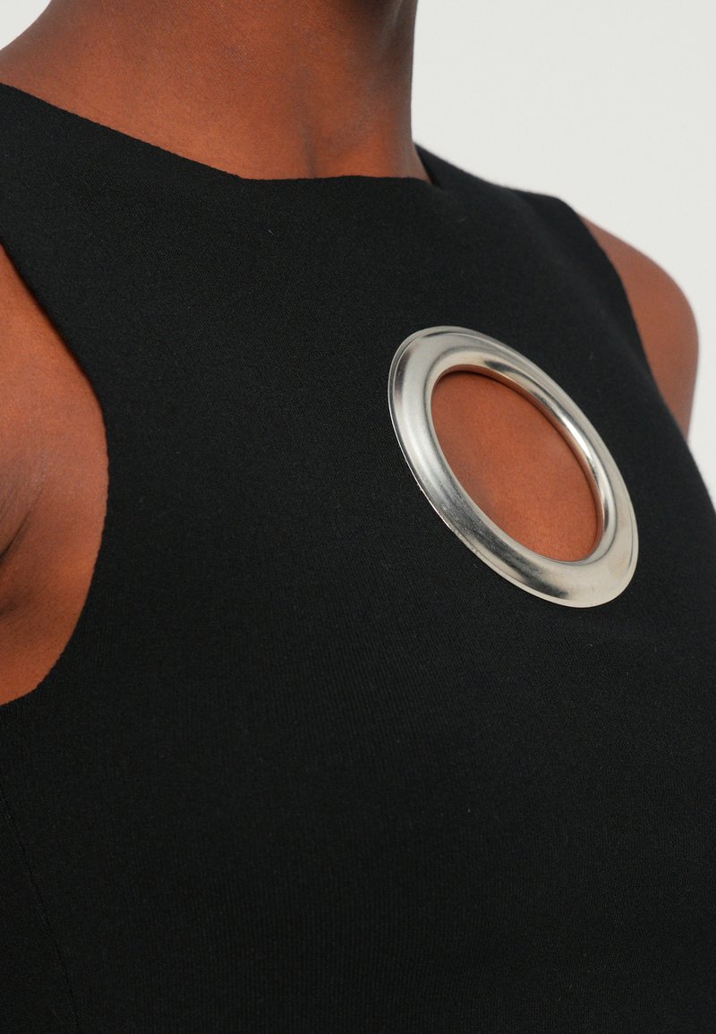 Black sleeveless top featuring a large silver circular accent at the neckline. Smooth texture with a fitted design.