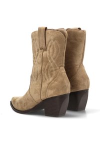 Botas de ante beige estilo western con un patrón de costura, punta redondeada y un tacón de madera apilada. Cuentan con tiradores para facilitar su uso.