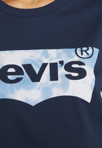 Tmavě námořnická modrá bavlněná tričko s bílým a světle modrým textovým grafickým prvkem, který zobrazuje značku "levi's" v tučných písmenech na pozadí mrakového vzoru.