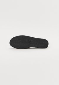 Suola di scarpa in gomma nera con motivi testurizzati per una migliore presa. Punta leggermente arrotondata e design piatto, con una stampa del logo vicino al tallone.