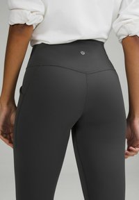 Czarne legginsy z wysokim stanem, wykonane z elastycznego materiału, charakteryzujące się gładką teksturą, bocznymi kieszeniami oraz małym logo na pasku.