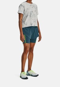 Camiseta gris con efecto tie-dye, pantalones cortos azules con acentos en verde neón y zapatillas de deporte ligeras con un diseño estampado.