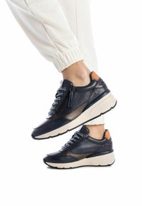 Zapatillas de cuero azul marino con acentos texturizados, que presentan una cremallera, cordones redondos y una suela color crema. Un detalle en marrón claro en la parte trasera añade contraste.