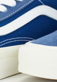 Gros plan de baskets en toile bleue avec semelles en caoutchouc blanches et un détail de bande ondulée blanche sur le côté.