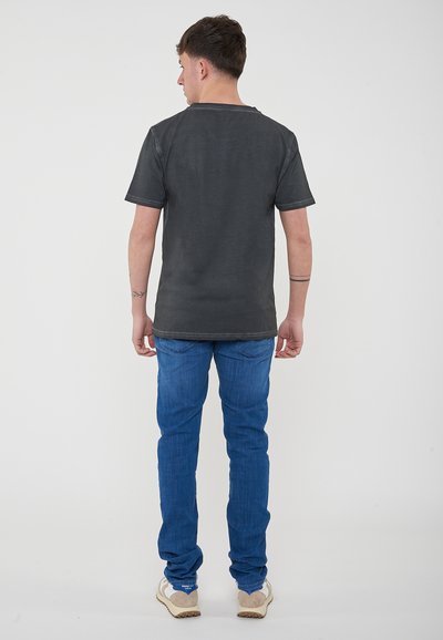 T-shirt grigio scuro con maniche corte e scollo rotondo, abbinato a jeans blu in denim e sneakers color crema. Tessuto morbido e vestibilità casual.