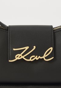 Black leather handbag featuring a textured finish and a prominent gold "Karl" signature on the front, with a zipper closure along the edge.