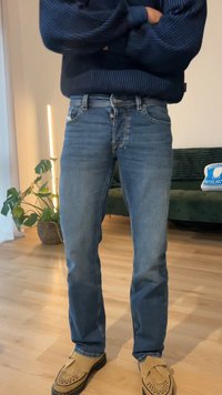 Blå jeans i denim med klassisk skärning, med fem fickor, knappstängning och lätt blekning. Bärs med beige mockasinliknande skor.