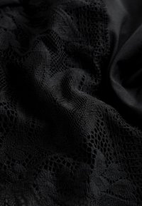 Čierna čipka s kvetinovými vzormi a jemnou sieťovanou textúrou, zahalená tak, aby sa ukázali záhyby a tiene.