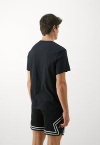 Black crew-neck t-shirt made of cotton, with short sleeves; worn with black shorts featuring white geometric accents and a mesh texture.