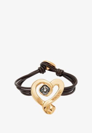 Colgante en forma de corazón de oro con una piedra negra facetada, sobre un cordón de cuero marrón. Presenta un acabado suave y un diseño entrelazado.