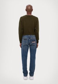 Maglione cropped verde oliva con scollatura tonda, abbinato a jeans a gamba dritta azzurri chiari con una patch "COUTURE" sulla tasca posteriore.