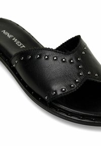 Pantofole nere in pelle, con un design aperto e arrotondato sulla punta, arricchite da occhielli in argento lungo i bordi e una suola piatta.