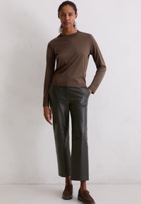 Bruine lange mouwen top gecombineerd met donkergroene leren wijde broek. De outfit heeft een ronde halslijn en een aansluitende pasvorm met minimale naden.