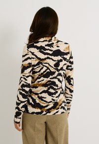 P camiseta de manga larga con un patrón de estampado animal en beige, negro y marrón, hecha de un material suave, con un diseño ajustado y escote redondo.