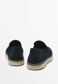 Černé semišové espadrilky s tkanou juteovou podrážkou. Design na obuv bez zapínání má zaoblenou zadní část a hladký povrch.