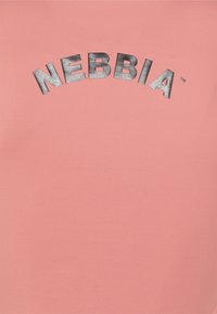 Lyserød bomulds t-shirt med ordet "NEBBIA" i metallisk sølv, der buer over den øverste del i en fed, blokskrift.