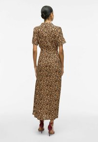 Robe maxi en imprimé léopard avec des manches courtes, un col, une taille cintrée et un tissu texturé. Portée avec des talons rouges à sangle au niveau de la cheville.