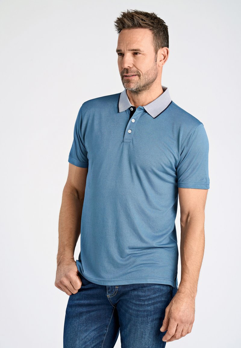 Blå pikétröja med grå krage och svarta detaljer, med korta ärmar och en avslappnad passform, parat med mörka jeans.