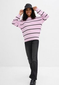 Maglione a righe rosa con strisce orizzontali nere, vestibilità comoda. Abbinato a jeans grigio scuro e un cappello a secchiello nero. Calzature nere.