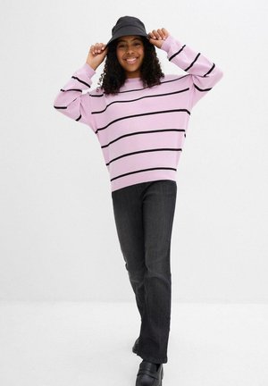 Maglione a righe rosa con strisce orizzontali nere, vestibilità comoda. Abbinato a jeans grigio scuro e un cappello a secchiello nero. Calzature nere.