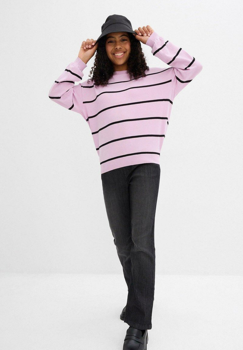 Maglione a righe rosa con strisce orizzontali nere, vestibilità comoda. Abbinato a jeans grigio scuro e un cappello a secchiello nero. Calzature nere.