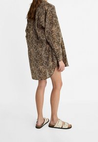 Šaty košilového střihu s leopardím potiskem, dlouhými rukávy a volným střihem, vyrobené z lehkého materiálu. V kombinaci se béžovými žabkami se dvěma přezkami.