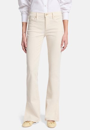 Witte flared jeans met een gladde textuur, vijf zakken, ritssluiting en goudkleurige hardware. Gecombineerd met lichtgele schoenen.